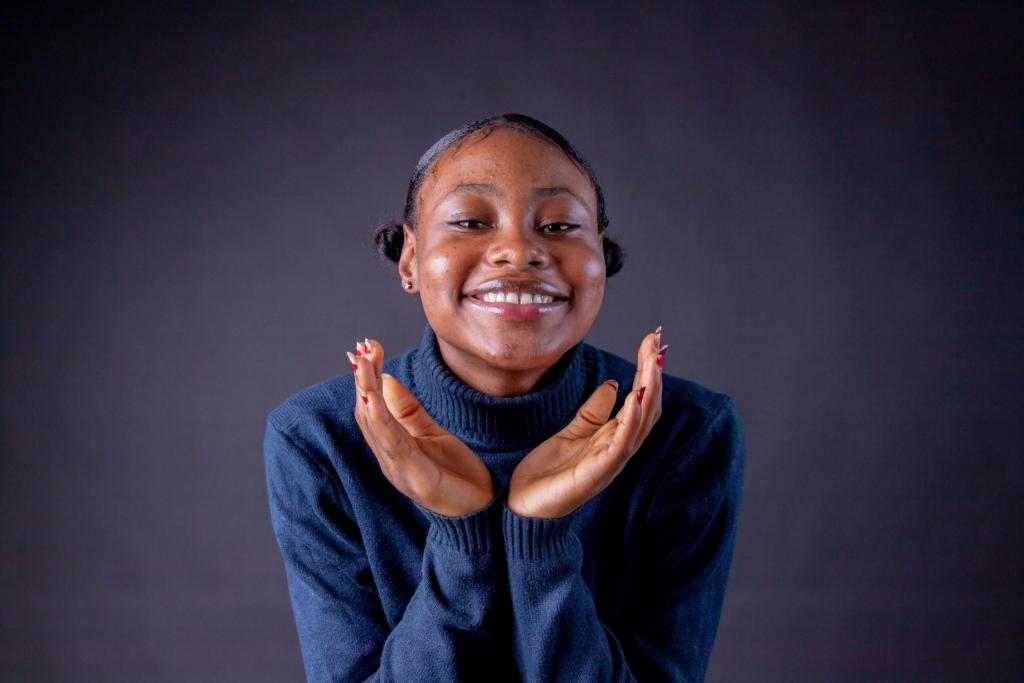 pexels-photo-10294305-10294305 Smiling woman in a blue sweater with hands on chin, conveying happiness and warmth.